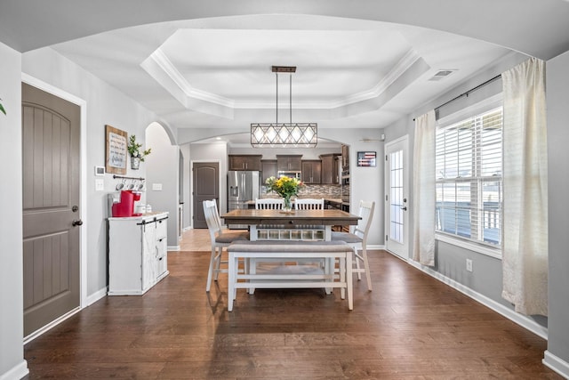 dining space featuring a tray ceiling, visible vents, dark wood finished floors, and arched walkways