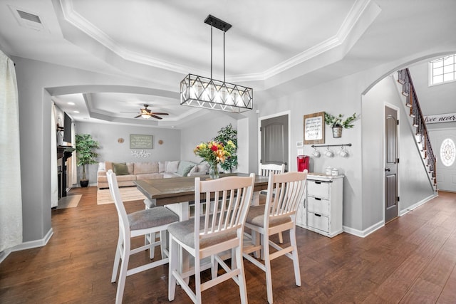 dining space featuring arched walkways, visible vents, stairs, a tray ceiling, and dark wood finished floors