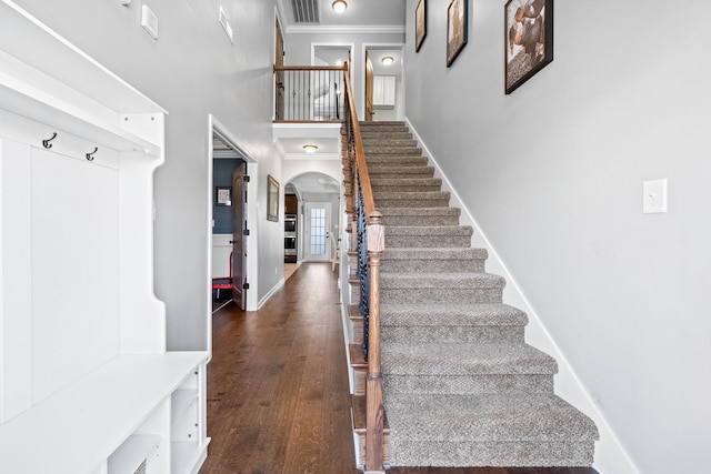 stairway featuring arched walkways, visible vents, hardwood / wood-style floors, ornamental molding, and baseboards