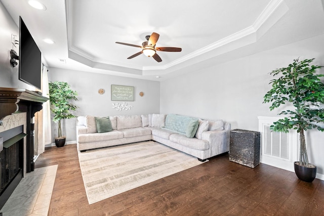 living area featuring a tray ceiling, a fireplace, crown molding, ceiling fan, and wood finished floors