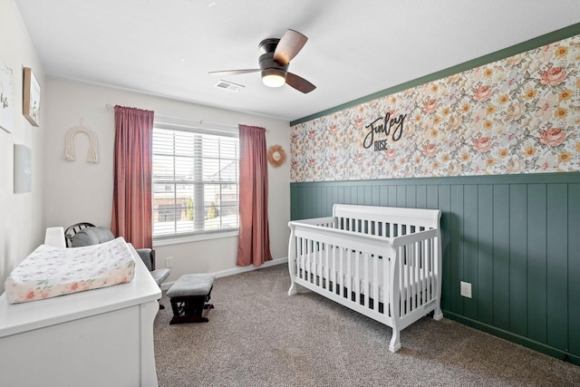 bedroom featuring a wainscoted wall, carpet floors, visible vents, a nursery area, and wallpapered walls