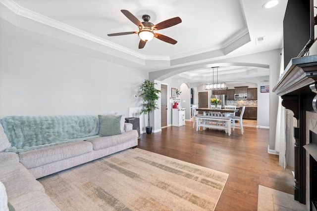 living room with arched walkways, visible vents, dark wood-style floors, a tray ceiling, and crown molding