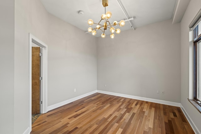 unfurnished room with a chandelier, wood finished floors, and baseboards