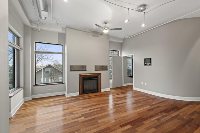 unfurnished living room with a fireplace, ceiling fan, track lighting, wood finished floors, and baseboards