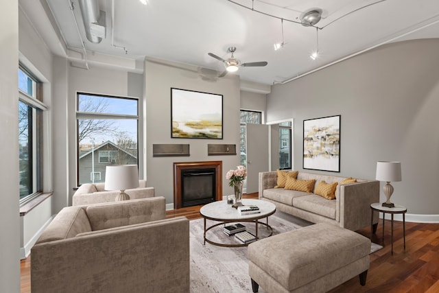 living area with attic access, baseboards, a glass covered fireplace, ceiling fan, and wood finished floors