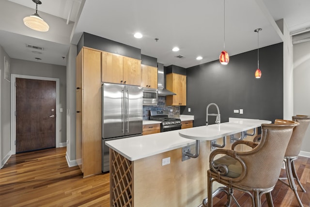 kitchen featuring light wood finished floors, stainless steel appliances, light countertops, visible vents, and wall chimney range hood