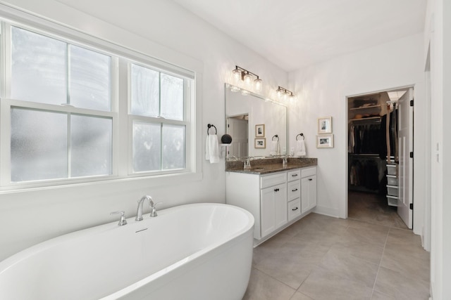 full bathroom with double vanity, tile patterned flooring, a spacious closet, a freestanding bath, and a sink