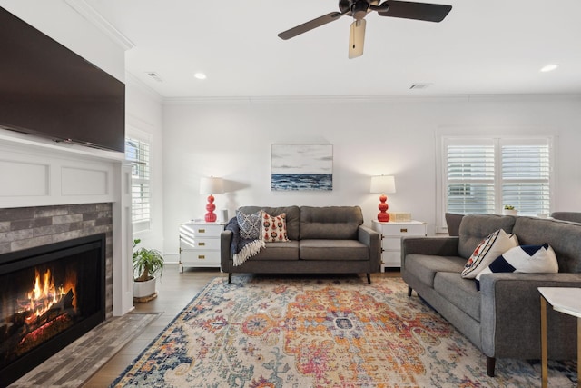 living room with a fireplace with flush hearth, visible vents, crown molding, and wood finished floors