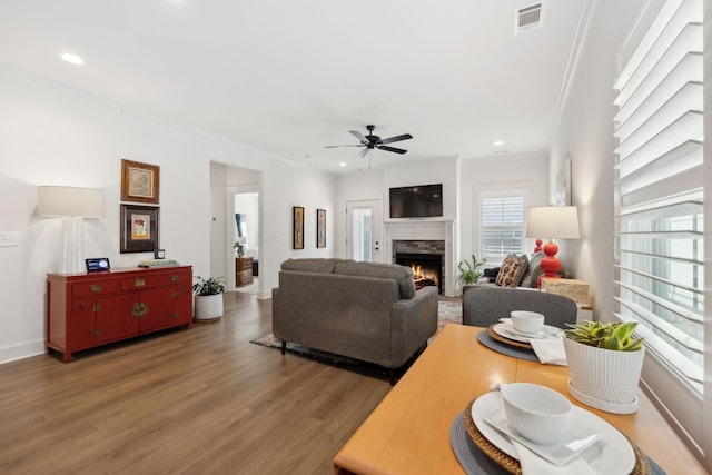 living area with a lit fireplace, visible vents, crown molding, and wood finished floors