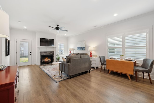 living room with crown molding, recessed lighting, light wood-style floors, ceiling fan, and a lit fireplace