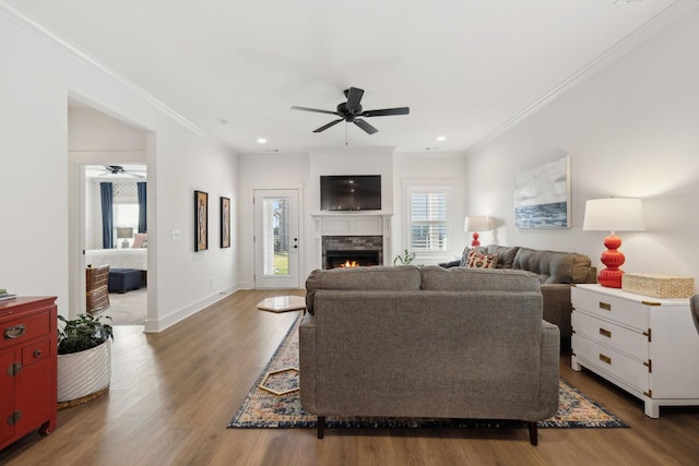 living room featuring a warm lit fireplace, baseboards, wood finished floors, and crown molding