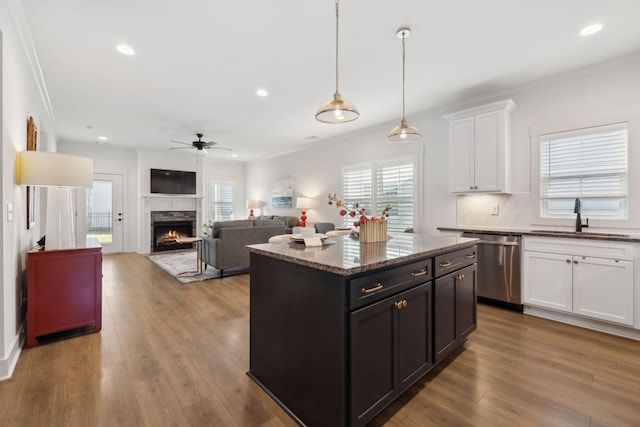 kitchen featuring dishwasher, wood finished floors, a lit fireplace, white cabinetry, and a sink