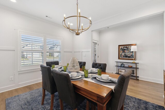 dining space with a chandelier, ornamental molding, and wood finished floors