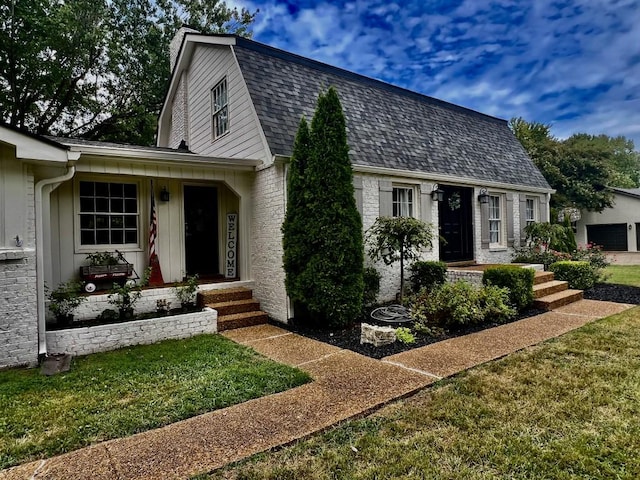 colonial inspired home with brick siding, a front lawn, a gambrel roof, and roof with shingles