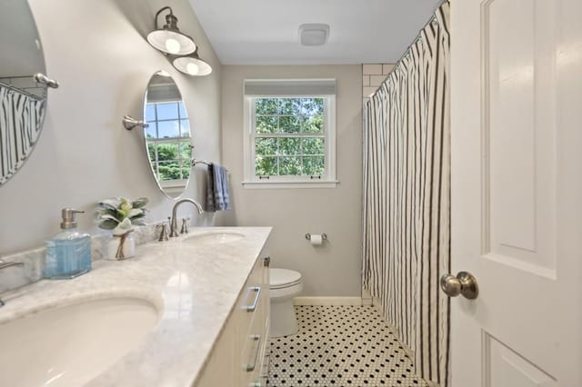 full bathroom with toilet, double vanity, baseboards, and a sink