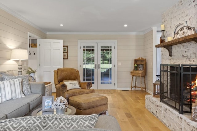 living room with ornamental molding, french doors, a large fireplace, and light wood-style flooring