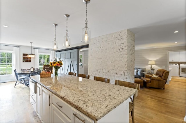 kitchen with a barn door, a breakfast bar area, light wood-style flooring, white cabinetry, and independent washer and dryer