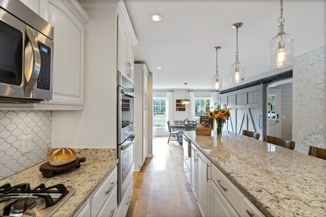 kitchen featuring light stone counters, light wood finished floors, tasteful backsplash, appliances with stainless steel finishes, and white cabinets