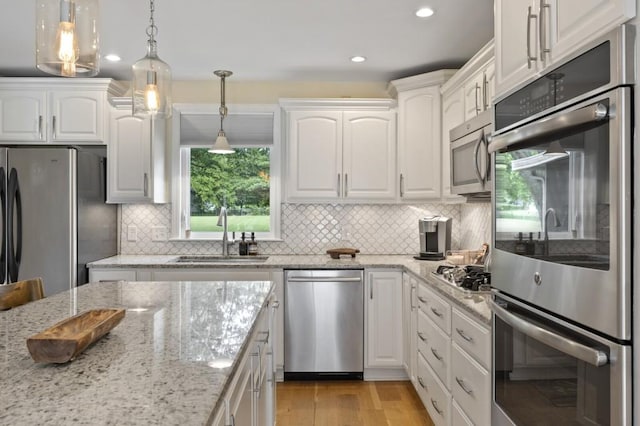 kitchen with light wood-style floors, appliances with stainless steel finishes, white cabinets, and a sink