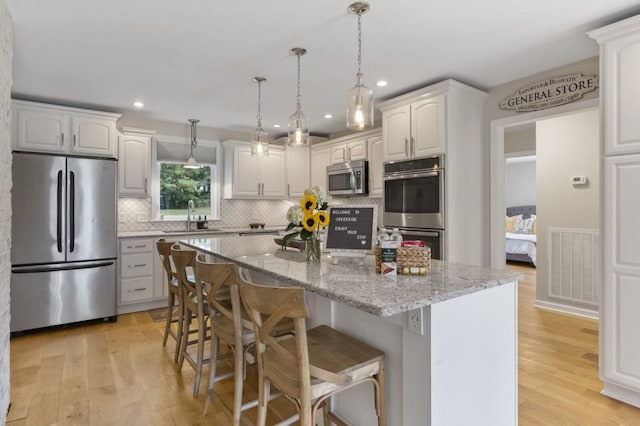 kitchen with appliances with stainless steel finishes, light stone counters, a center island, light wood-style floors, and a sink