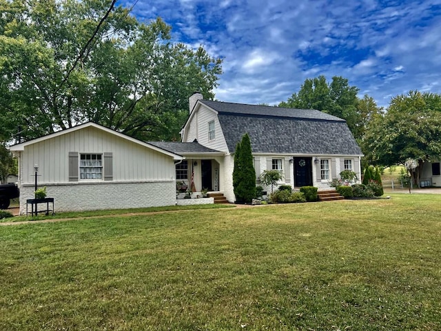 colonial inspired home featuring brick siding, a shingled roof, a gambrel roof, a front yard, and a chimney