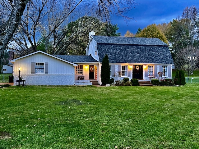 colonial inspired home with a shingled roof, a front yard, a chimney, and a gambrel roof