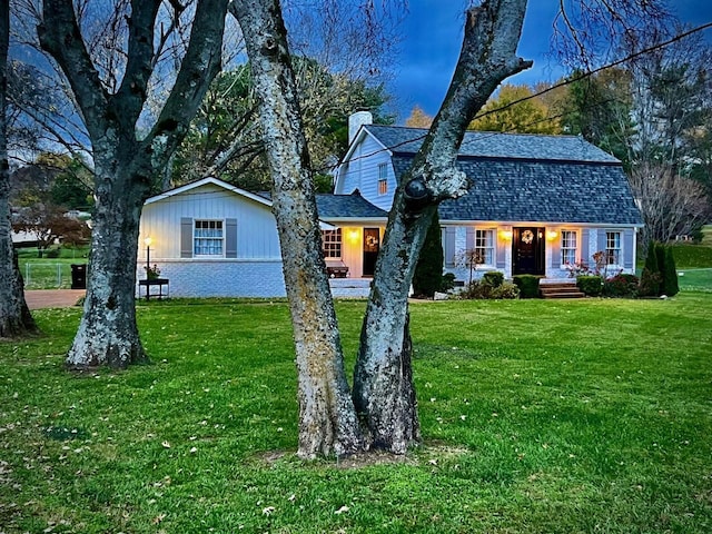 colonial inspired home with brick siding, a shingled roof, a gambrel roof, a front yard, and a chimney