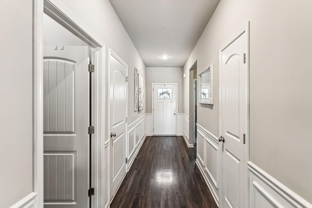 hall with dark wood-type flooring, wainscoting, and a decorative wall