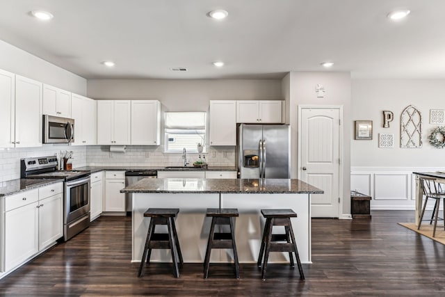 kitchen with a breakfast bar, a kitchen island, a sink, appliances with stainless steel finishes, and tasteful backsplash