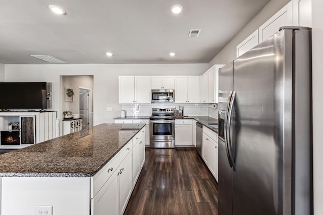 kitchen with tasteful backsplash, white cabinets, dark wood-style flooring, a center island, and stainless steel appliances