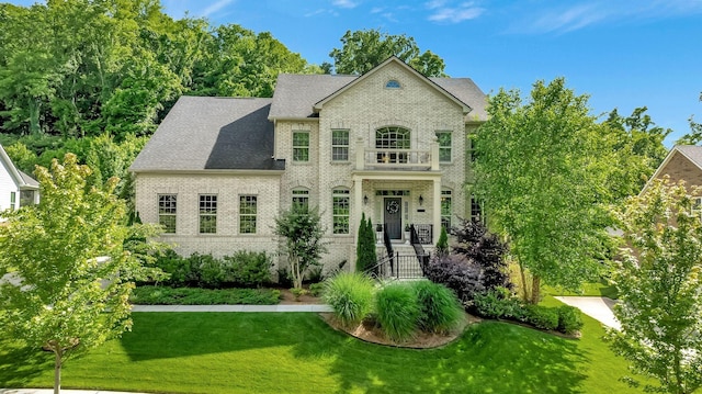 view of front of property with a shingled roof, a front yard, and brick siding