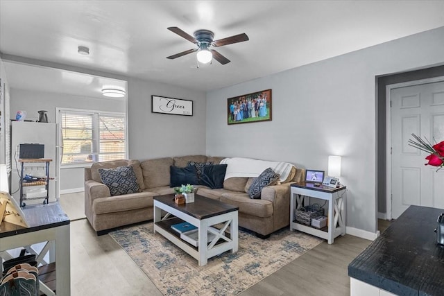 living room featuring light wood-type flooring, baseboards, and a ceiling fan