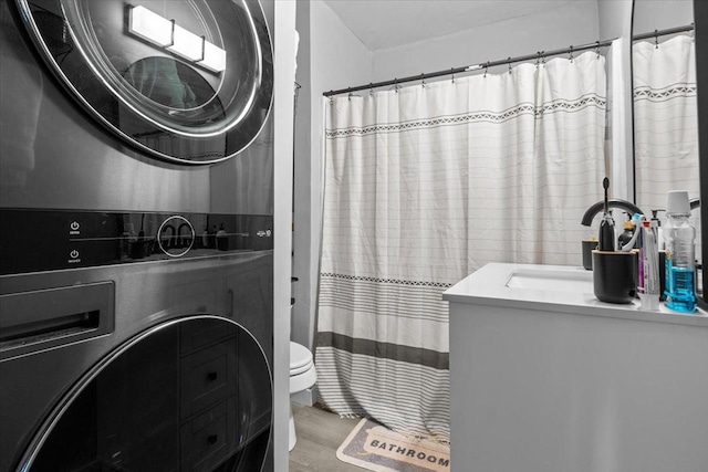 full bath featuring a shower with shower curtain, toilet, stacked washer and clothes dryer, wood finished floors, and vanity