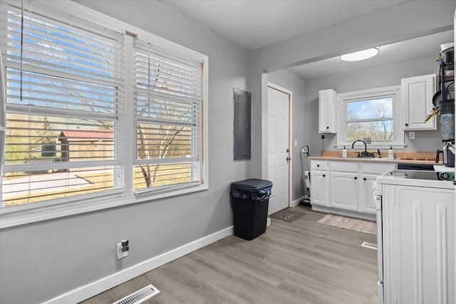 kitchen with stove, visible vents, baseboards, white cabinets, and light wood finished floors