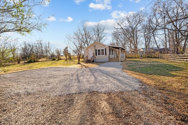 view of side of home with entry steps, a lawn, gravel driveway, and fence