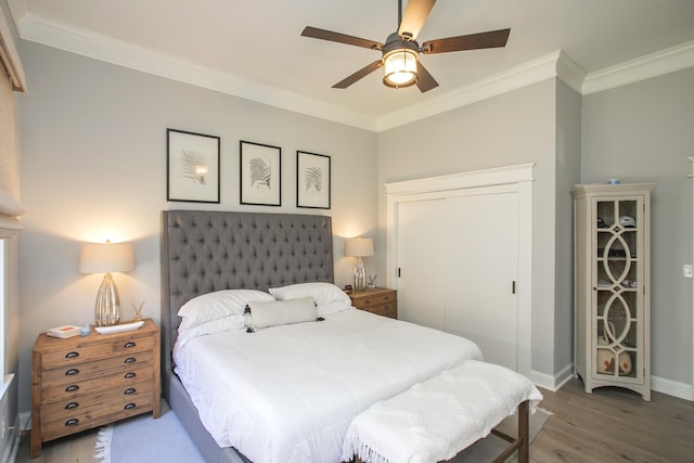 bedroom featuring wood finished floors, a ceiling fan, baseboards, ornamental molding, and a closet