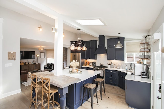 kitchen with a breakfast bar area, premium range hood, light countertops, appliances with stainless steel finishes, and lofted ceiling with skylight