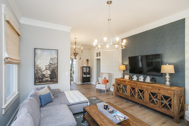 living room featuring an accent wall, wood finished floors, wallpapered walls, an inviting chandelier, and crown molding