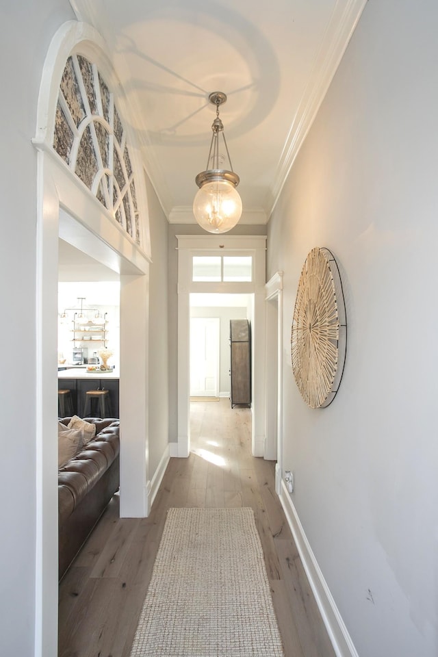 corridor with wood-type flooring, ornamental molding, a chandelier, and baseboards