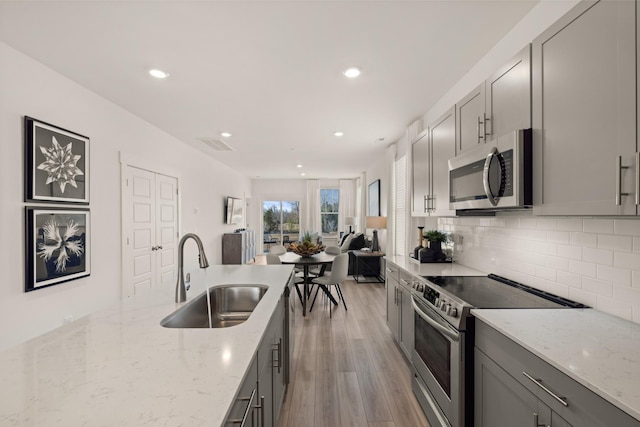 kitchen with gray cabinets, decorative backsplash, stainless steel appliances, and a sink