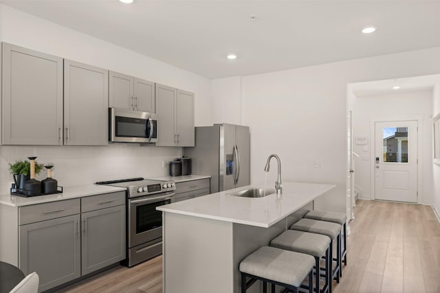 kitchen with a breakfast bar area, gray cabinetry, stainless steel appliances, a sink, and light wood-style floors