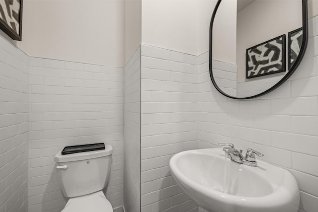 half bathroom with toilet, a sink, and tile walls