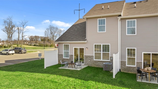 rear view of house featuring a patio, cooling unit, brick siding, a shingled roof, and a lawn