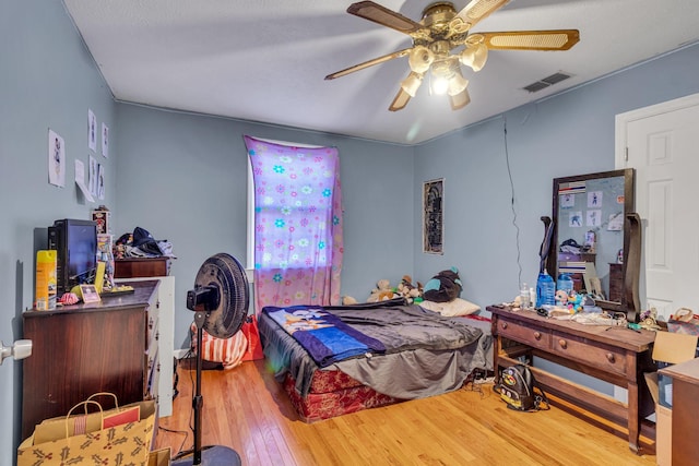 bedroom with ceiling fan, visible vents, and wood finished floors