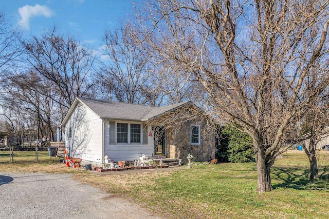 view of front of house featuring roof with shingles, a front yard, fence, stone siding, and driveway