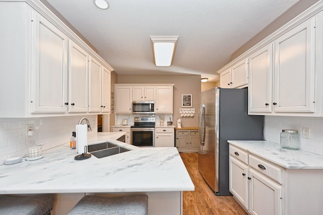 kitchen featuring a breakfast bar, appliances with stainless steel finishes, a sink, light wood-type flooring, and a peninsula