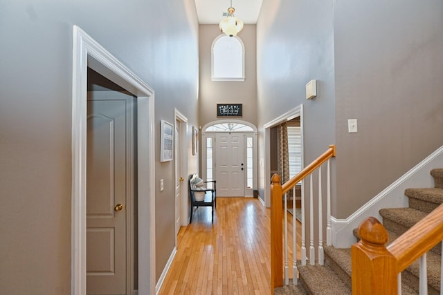 foyer entrance with light wood-style floors, baseboards, stairway, and a towering ceiling