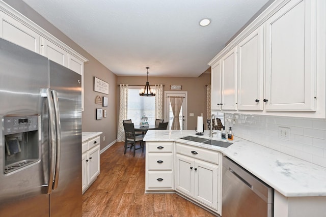 kitchen featuring a peninsula, a sink, stainless steel appliances, light wood-style floors, and backsplash