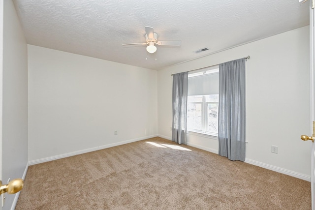 carpeted empty room with ceiling fan, a textured ceiling, visible vents, and baseboards