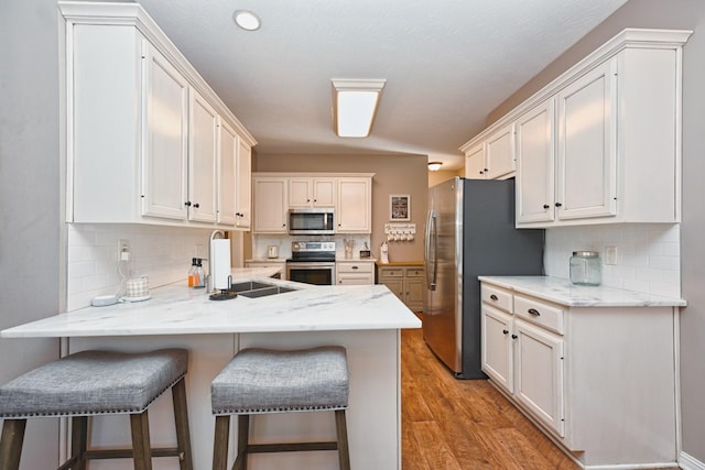 kitchen with a breakfast bar area, stainless steel appliances, a peninsula, a sink, and light wood finished floors